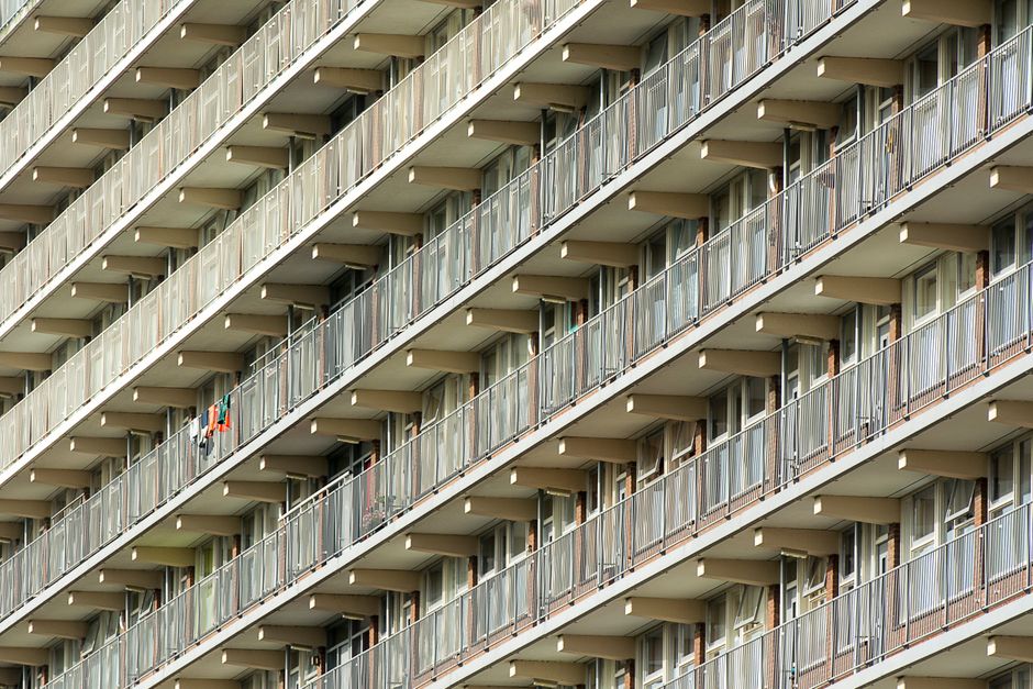 Photograph of a multi-storey residential building on Stockwell Park Estate, with beige and light blue facades. The building features numerous rectangular windows, some with visible curtains or blinds,