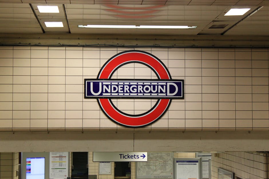 Close-up of a white tiled wall at Stockwell tube station featuring a large red and blue London Underground roundel sign with the word 'UNDERGROUND' prominently displayed. Below the sign, there is a wh