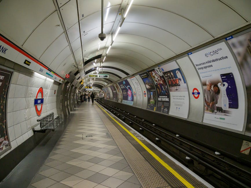 Close-up of a white tiled wall at Stockwell tube station featuring a large red and blue London Underground roundel sign with the word 'UNDERGROUND' prominently displayed. Below the sign, there is a wh